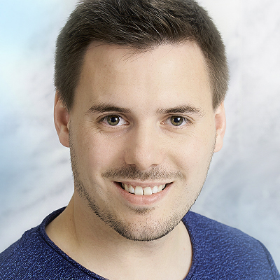 Clemens Faustenhammer mit kurzen braunen Haaren und Bartstoppeln, der ein blaues Hemd trägt, lächelt vor einem hellen, wolkigen Hintergrund in die Kamera - perfekt für professionelle Referentenprofile.