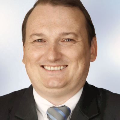 Marcus Ruhnau im Anzug und mit blau gestreifter Krawatte, der oft als einer der Top-Referenten gesehen wird, lächelt in die Kamera vor einem hellen, verschwommenen Hintergrund.