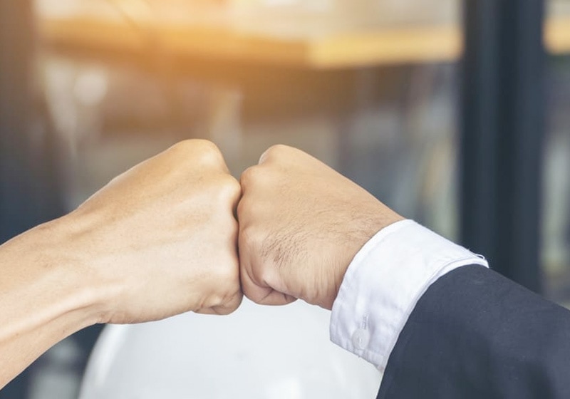 Two people, one in a suit and one in casual clothes, shake hands in a hall to celebrate the success of their stock return optimization program.