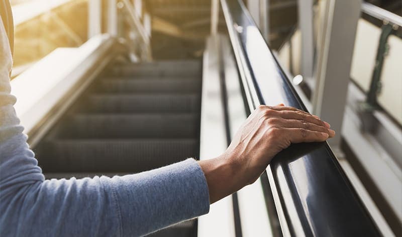The hand of a person holding the black handrail of an escalator, with the steps of the escalator visible in the background, symbolizes an upward journey, similar to navigating an optimization program to increase stock returns.
