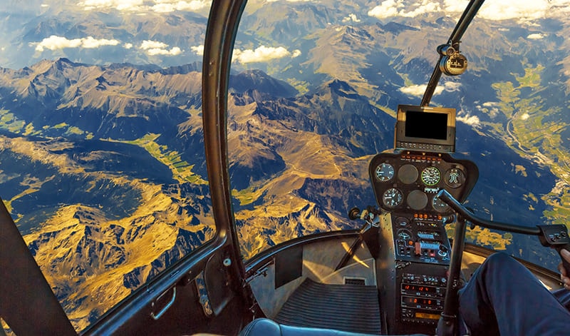 A view from the cockpit of a helicopter flying over mountainous terrain, with instrument panels and a landscape below - ideal for anyone interested in aviation and account management.
