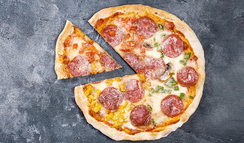 A whole pepperoni pizza, with one slice removed, rests on a dark gray surface - perfect for sharing and a delicious example of tradable produce.