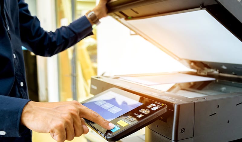 Eine Person, die das Touchscreen-Bedienfeld eines Fotokopierers bei geöffneter Kopiererklappe bedient und sich auf das Scannen oder Kopieren eines Dokuments vorbereitet, ähnlich wie ein ETF-Replikator, der Finanzaufgaben rationalisiert.