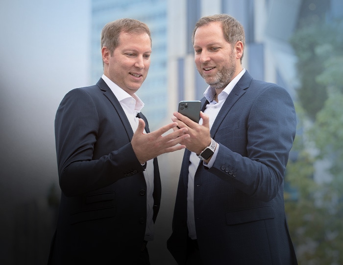 Die Geschäftsführer Andreas und Christian Weiß stehen im Freien, betrachten eine Imagebroschüre und besprechen Details mit einem Smartphone.