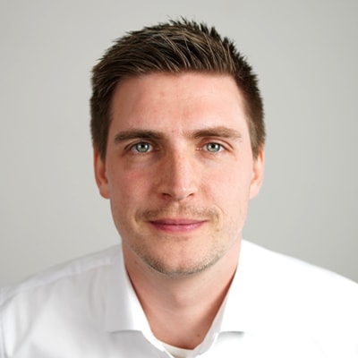 Referent Philipp Malte Lingnau mit kurzen braunen Haaren und heller Gesichtsbehaarung, bekleidet mit einem weißen Hemd, blickt in die Kamera vor einem schlichten hellen Hintergrund - perfekt für professionelle Referentenprofile.