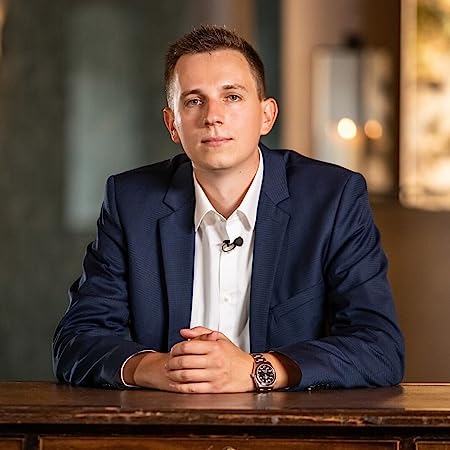 Moritz Hessel in a navy blue suit and white shirt sits at a wooden table with folded hands and looks into the camera in a softly lit interior, conveying professionalism - perfect for advertising Moritz Hessel's managed account and passive income solutions.