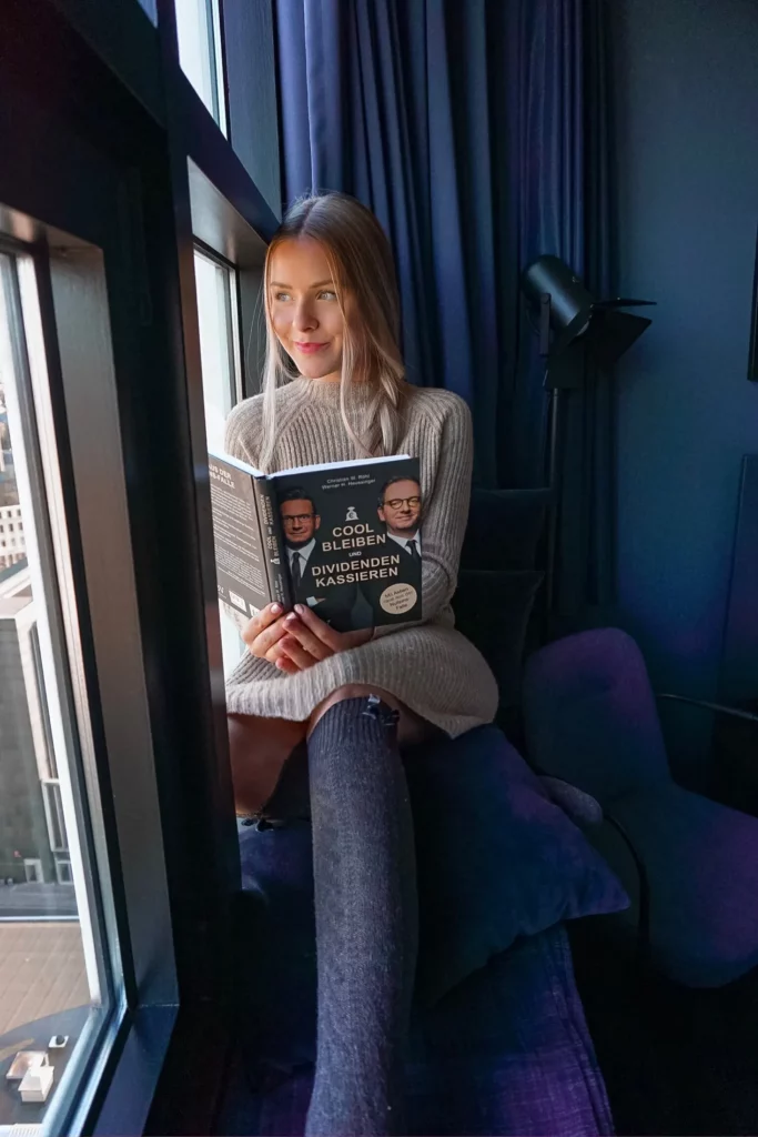Frau sitzt am Fenster und liest ein Buch bei gemütlicher Beleuchtung.
