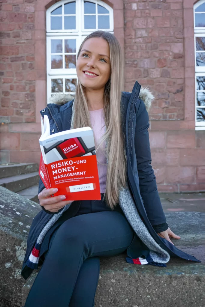 Eine Frau sitzt draußen und hält ein Buch über Risiko- und Geldmanagement in der Hand.