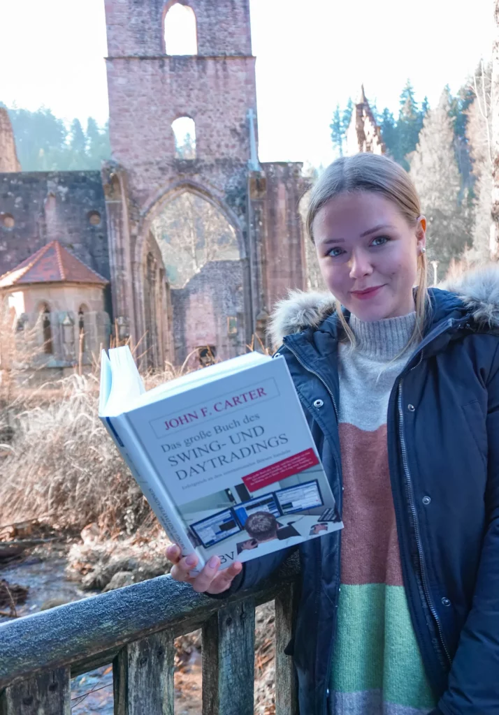 Eine Frau mit einem Buch steht vor den Ruinen eines alten gotischen Bauwerks.