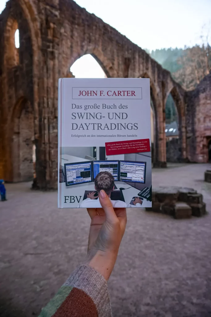 Eine Person hält ein Buch mit dem Titel „Das große Buch des Swing- und Daytradings“ von John F. Fuhrmann vor einem alten Torbogen.