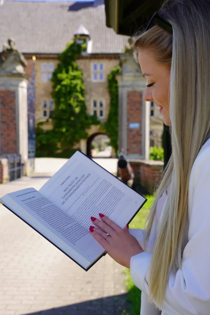Eine junge Frau liest ein Buch vor einem historischen Gebäude.