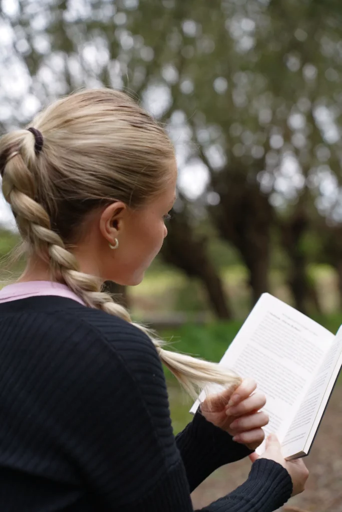 Frau liest ein Buch im Freien mit Bäumen im Hintergrund.