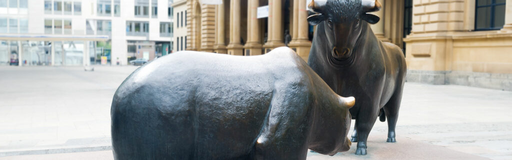Ein bronzener Bulle und eine Bärenstatue stehen sich auf einem Platz im Freien gegenüber und symbolisieren die Marktbewegungen, wie sie in DAX Analyse zu sehen sind. Moderne und klassische Gebäude bilden die Kulisse, die den Geist des finanziellen Allzeithochs heraufbeschwört.