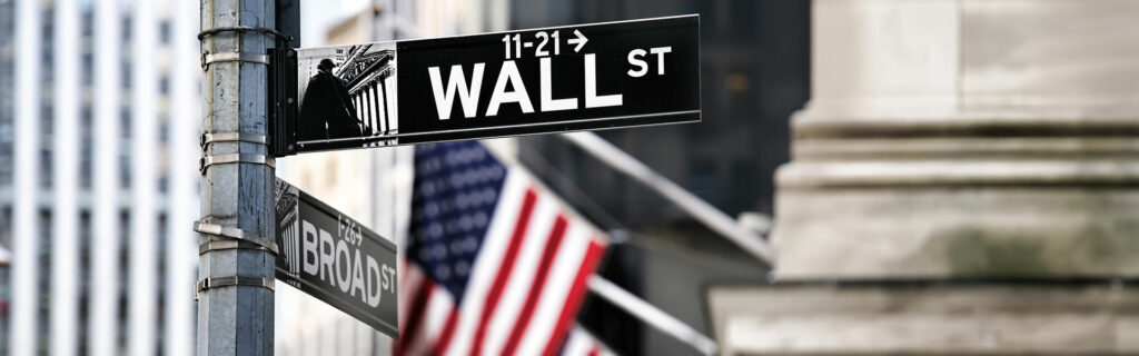 Straßenschilder für die Wall Street und die Broad Street an einer Kreuzung, mit einer amerikanischen Flagge und städtischen Gebäuden im Hintergrund - ein Hinweis auf den Puls der Finanzwelt inmitten von Comeback der Bullen und S&P 500 Analyse.