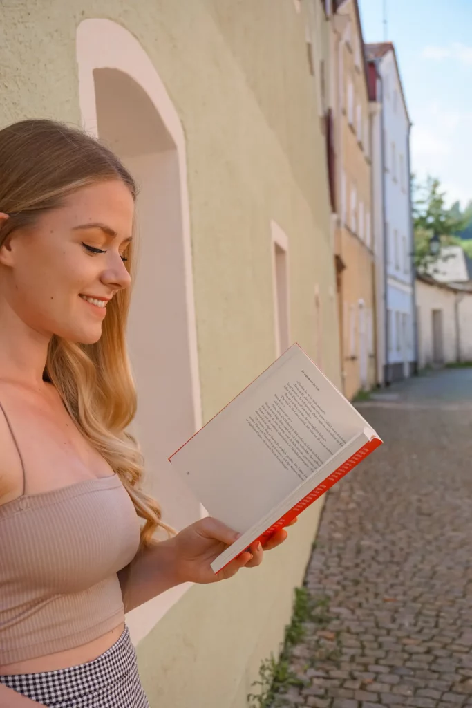 Young woman reading a book on a sunny cobblestone street.