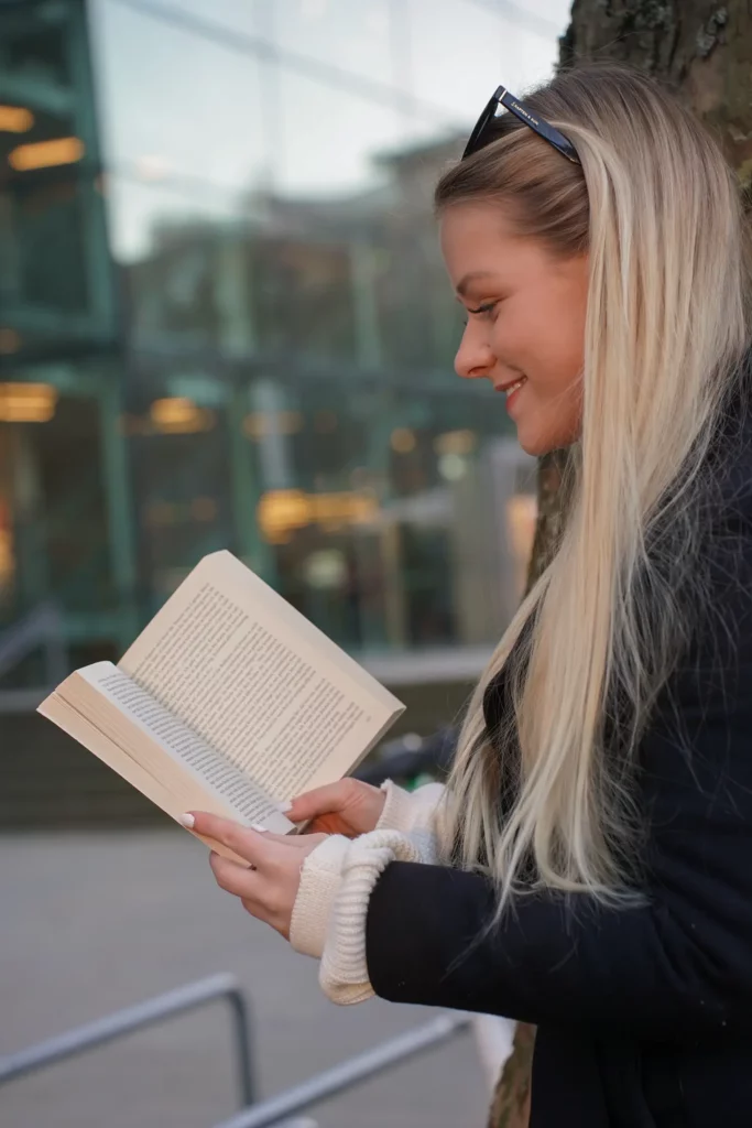 Eine Frau lächelt, während sie draußen ein Buch liest.