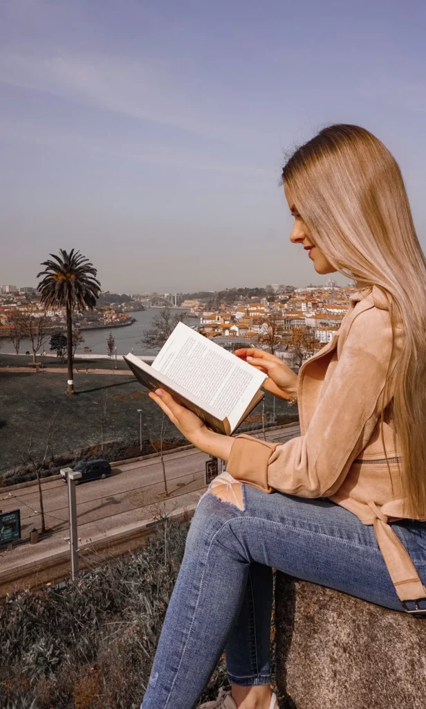Frau liest ein Buch im Freien vor einem malerischen Stadthintergrund.