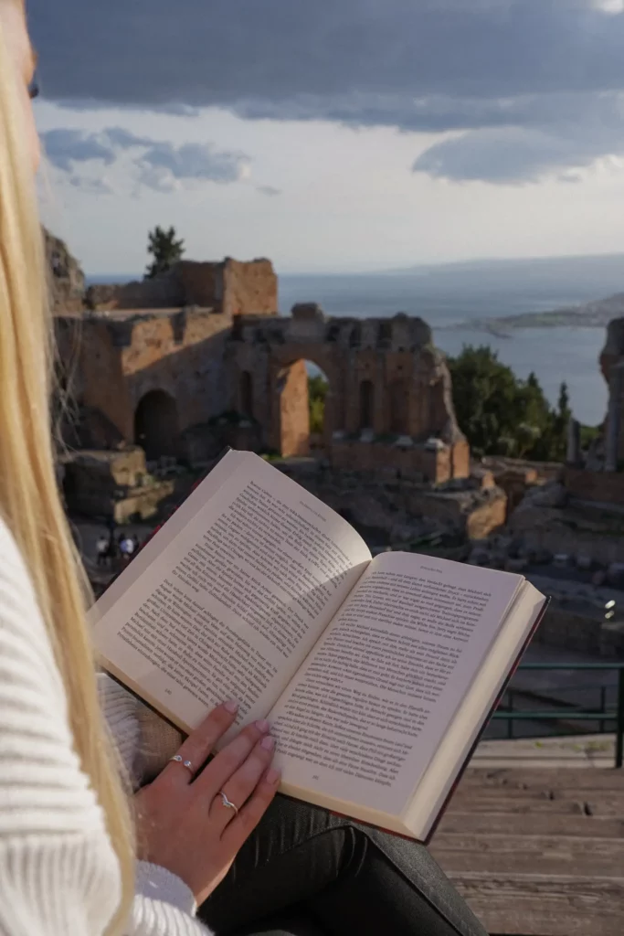 Frau liest ein Buch mit antiken Ruinen und einer malerischen Landschaft im Hintergrund.