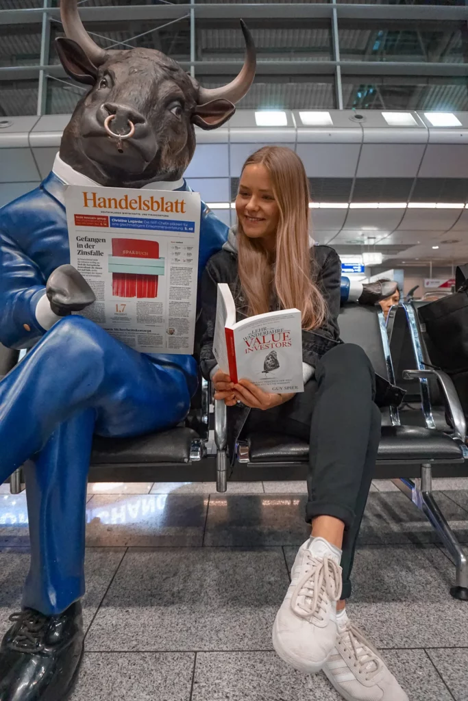 Eine Person sitzt neben einer Stierstatue und scheint im Wartebereich eines Flughafens Zeitung zu lesen.