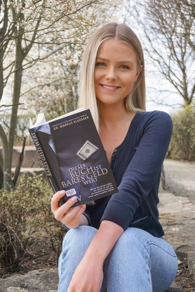 Eine Frau hält ein Buch in der Hand und lächelt in die Kamera.