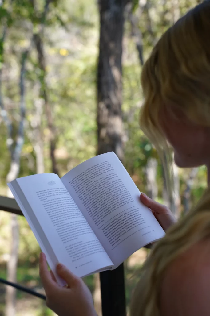 Eine Person ist in die Lektüre eines Buches im Freien, umgeben von Bäumen, vertieft.