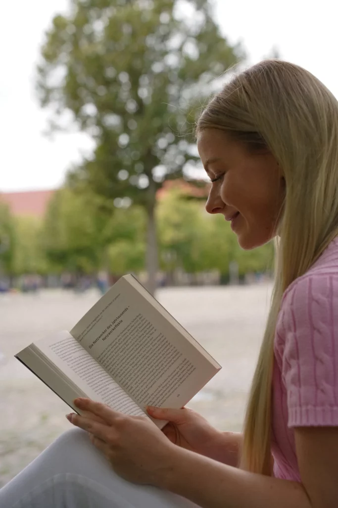 Frau liest ein Buch in einer Parklandschaft.