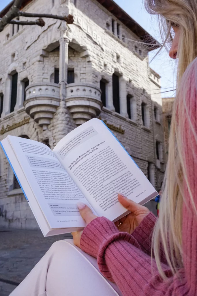 Frau liest ein Buch vor einem Steingebäude mit „Polibear“-Schild.