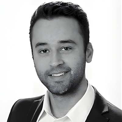 Sebastian Pahl in dunkler Anzugsjacke und weißem Hemd lächelt in die Kamera vor einem schlichten, hellen Hintergrund.