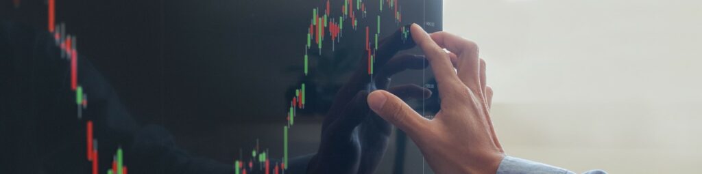 A person interacts with a large digital screen displaying a candlestick chart with green and red bars, commonly used for financial or stock market analysis and market technique trading strategies.