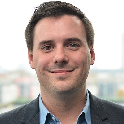 Ein professionelles Porträt eines lächelnden Mannes namens Clemens Faustenhammer in dunkler Jacke und blauem Hemd vor unscharfem Hintergrund.