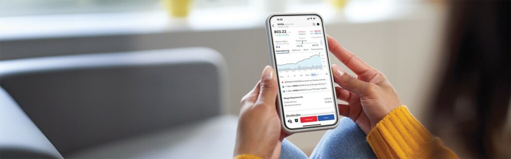 Eine Person hält ein Smartphone, auf dem eine Finanz-App mit Börseninformationen wie Kontostand, Aktienkursen und Charts angezeigt wird, während sie in einem Raum sitzt, im Hintergrund steht ein Sofa.