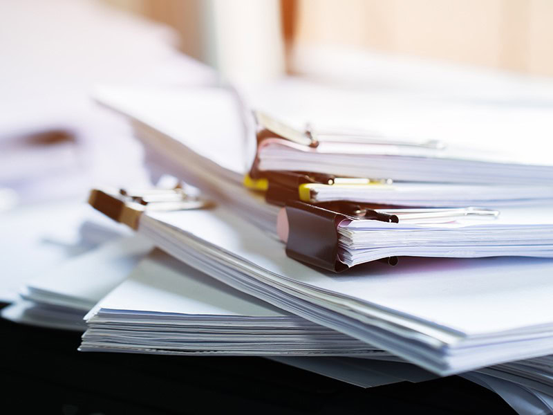 A jumbled pile of paper documents with staples lies on a desk waiting to be processed for tax filing.