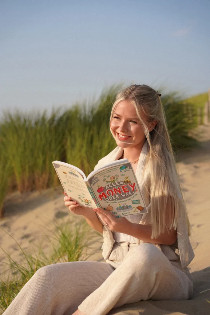 Eine Frau sitzt am Strand und liest ein Buch.
