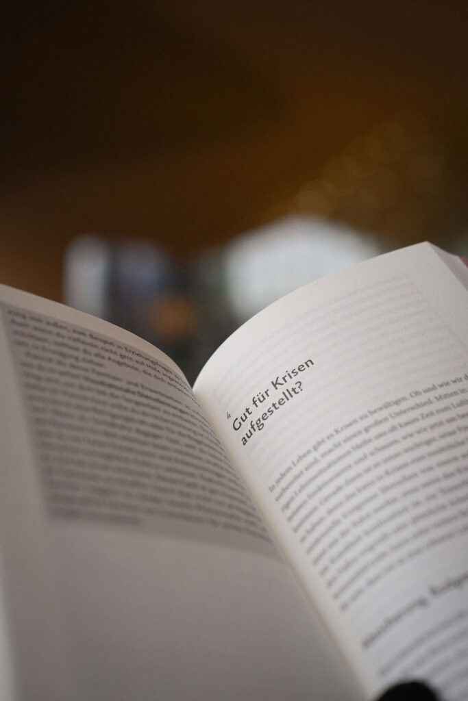 Offenes Buch mit schräg geneigtem Text in deutscher Sprache. Der Fokus der Seite liegt auf dem Satz „Gut für Krisen aufgestellt?“ in sanft beleuchteter Umgebung.