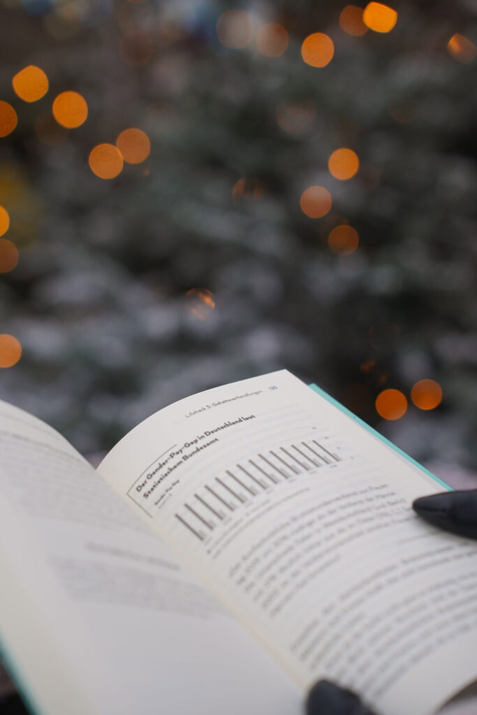 Eine Person liest im Freien ein Buch mit verschwommenen Lichtern im Hintergrund.