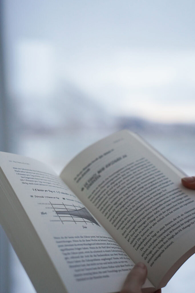 Hände halten ein offenes Buch mit Text und einem Diagramm auf den Seiten. Unscharfer Hintergrund.