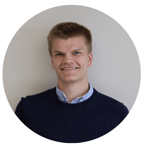 Christian Böttger with short, light brown hair, wearing a blue sweater over a collared shirt, smiles against a plain, light background.