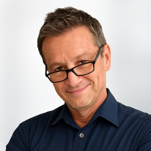 Referenten mittleren Alters mit kurzen braunen Haaren und Brille, die ein dunkelblaues Hemd mit Kragen tragen, lächeln in die Kamera vor einem schlichten hellen Hintergrund.