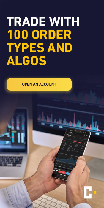 Person holding a smartphone with a trading app on the screen in front of computer monitors displaying financial charts; ad text promoting trading with 100 order types and algorithms.