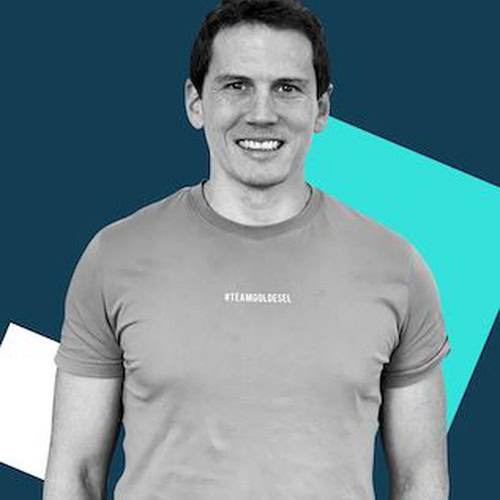 Ein Mann in einem taillierten T-Shirt steht lächelnd vor einem grafischen Hintergrund mit blauen und weißen geometrischen Formen.